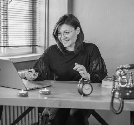 A young woman working on her laptop in a vintage-style office setting.