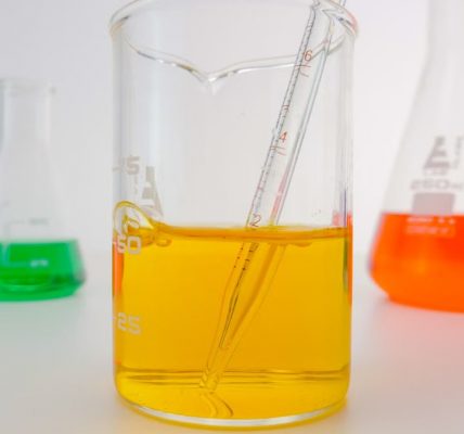 Close-up of vibrant chemical solutions in beakers with pipette in a lab setting.