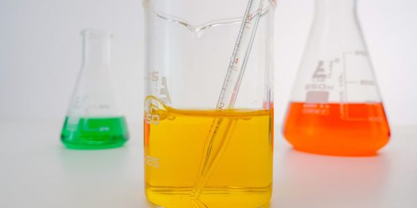Close-up of vibrant chemical solutions in beakers with pipette in a lab setting.